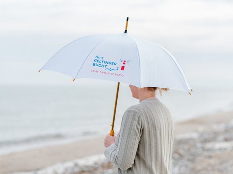 Frau mit weißem Regenschirm, auf dem "Amt Geltinger Bucht" geschrieben steht