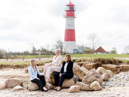 die 3 Standesbeamtinnen sitzend auf Steinen mit Leuchtturm im Hintergrund